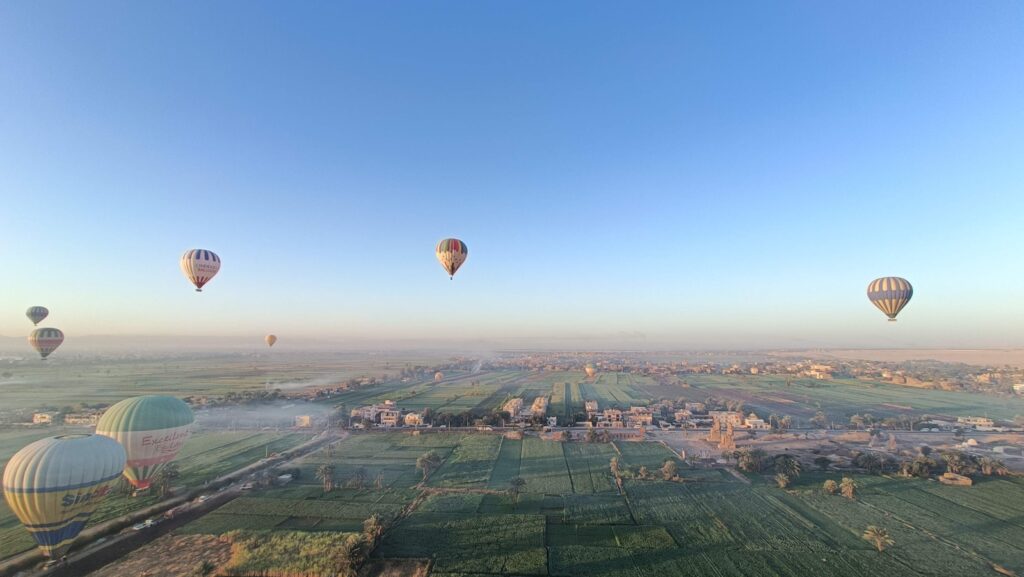 Hot air balloons floating over green fields in Luxor