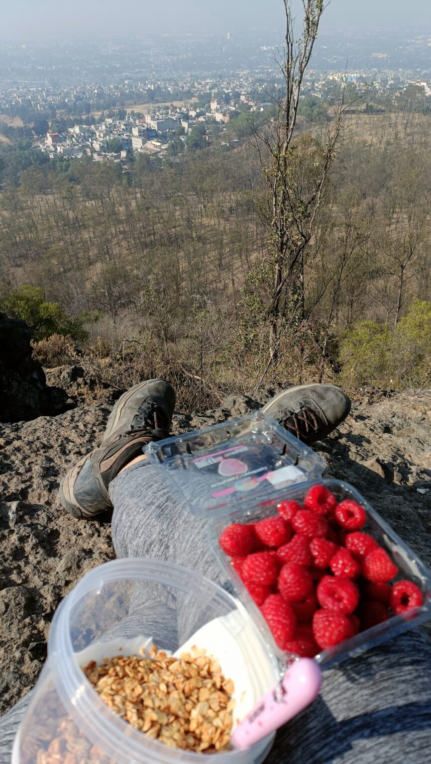 Hiking boots and a snack of raspberries and granola at a viewpoint over Mexico City