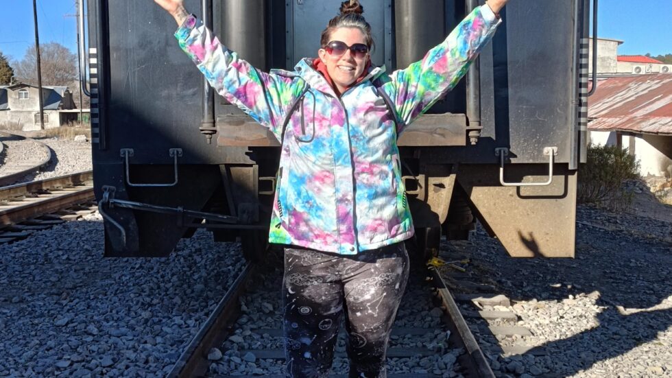 Hannah with arms raised on the tracks behind the El Chepe train