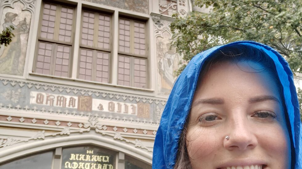 Hannah in a blue raincoat outside Livraria Lello in Porto