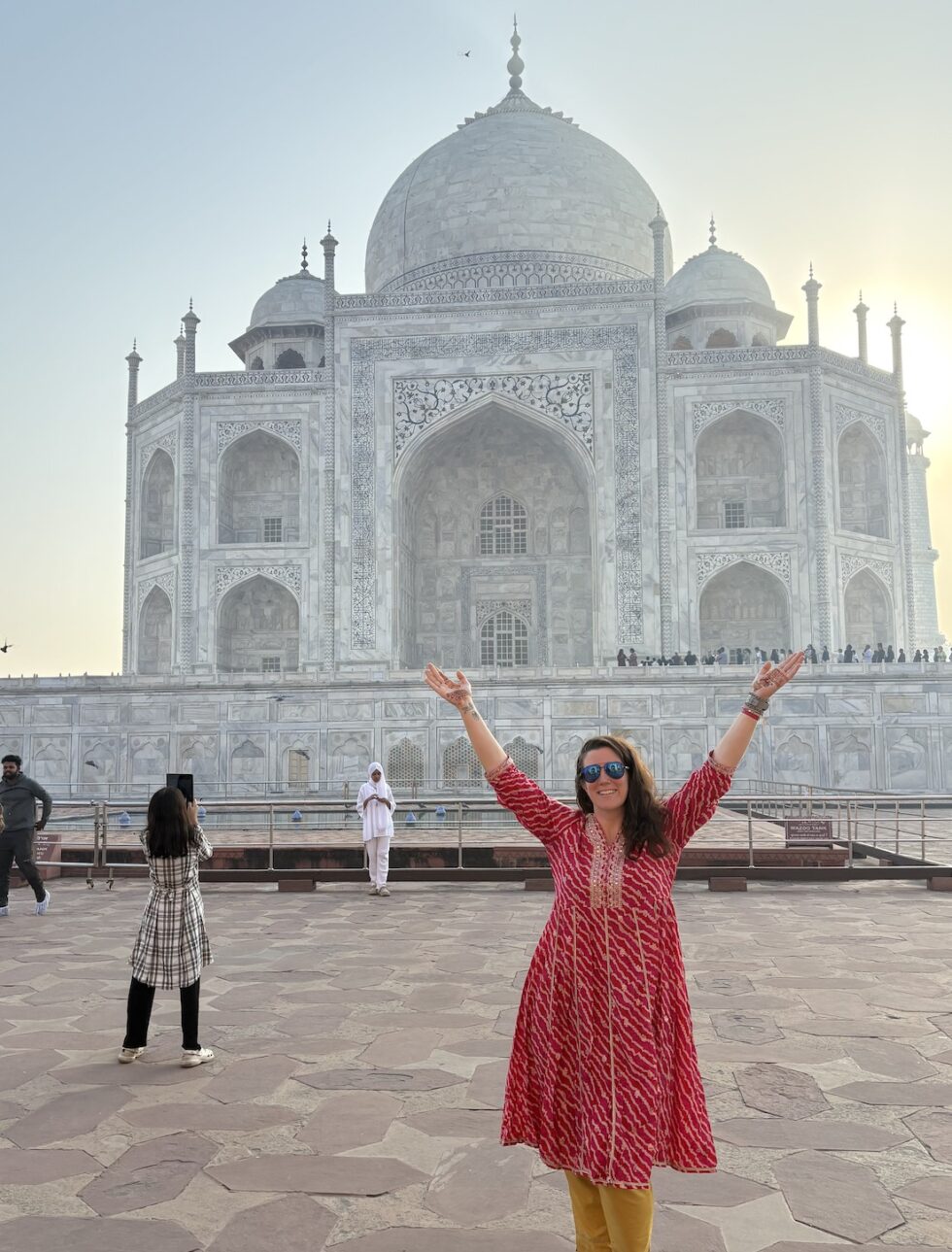 Hannah in a red dress with arms raised in front of the Taj Mahal