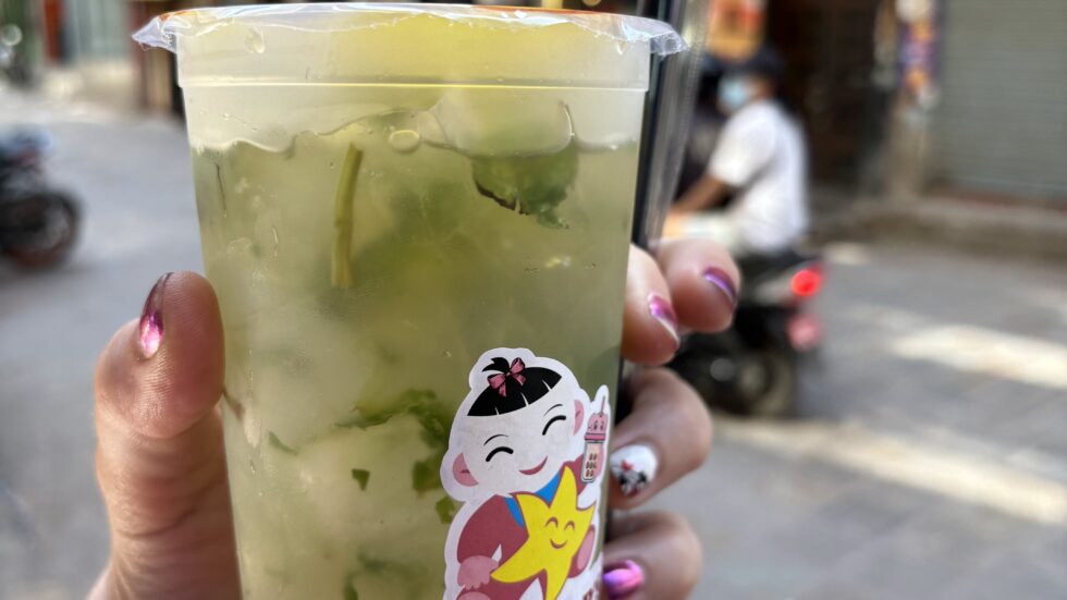 Hand holding an iced drink on a busy street in Kathmandu