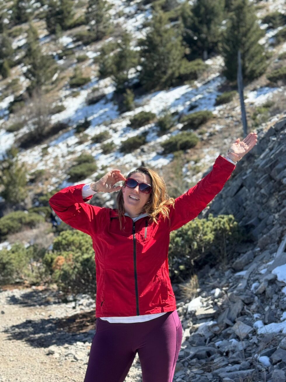 Hannah in a red jacket with arms raised on a snowy slope at La Marta