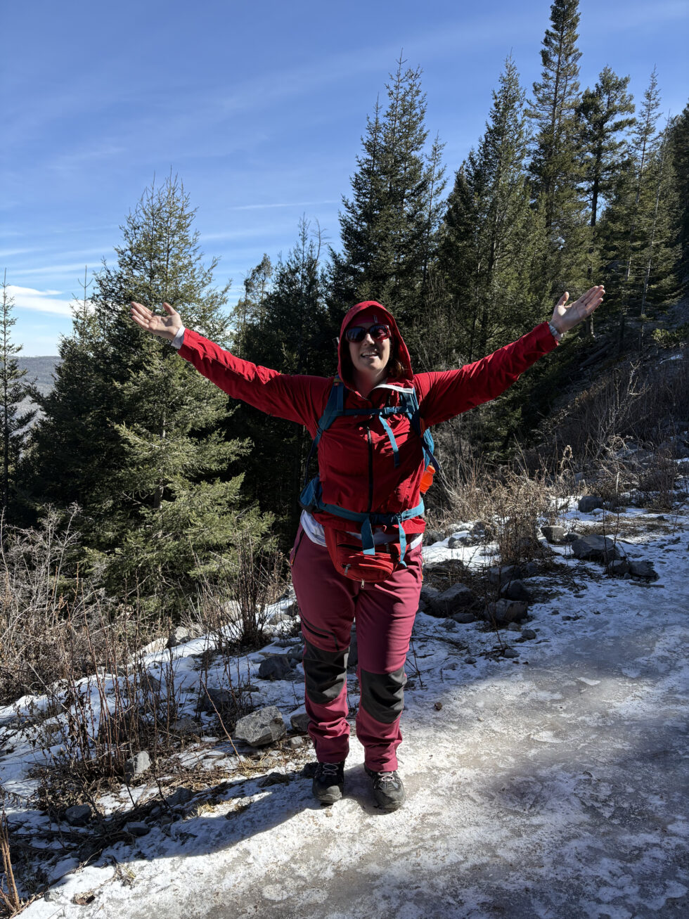 Hannah with arms raised on a snowy trail in the pine forest on La Marta