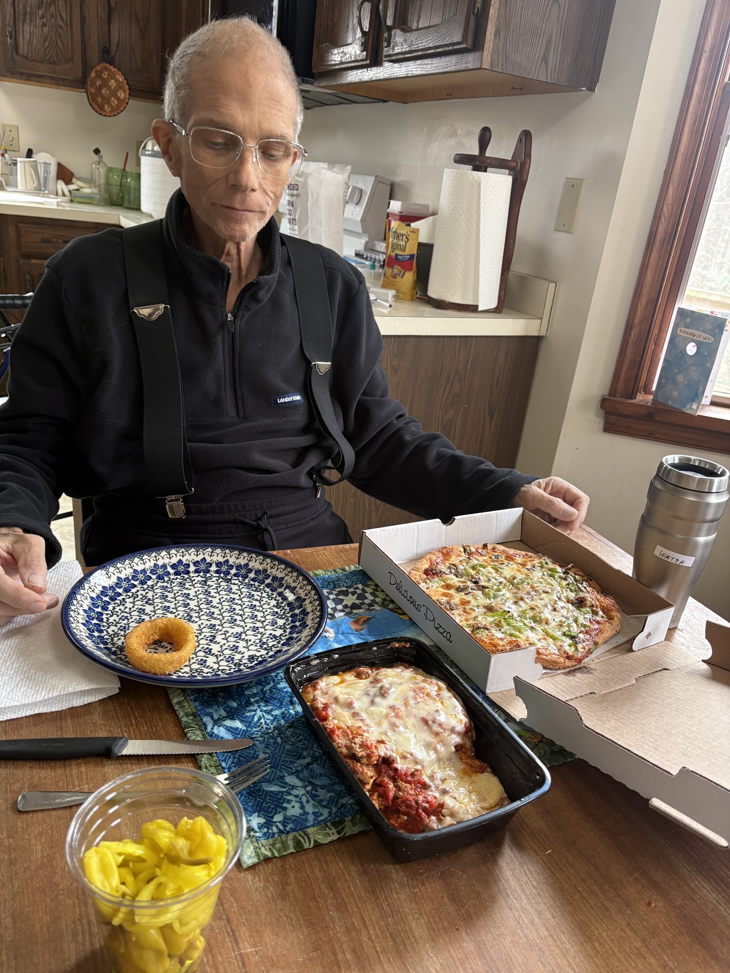 A man sitting at a kitchen table with a plate of food in front of him.