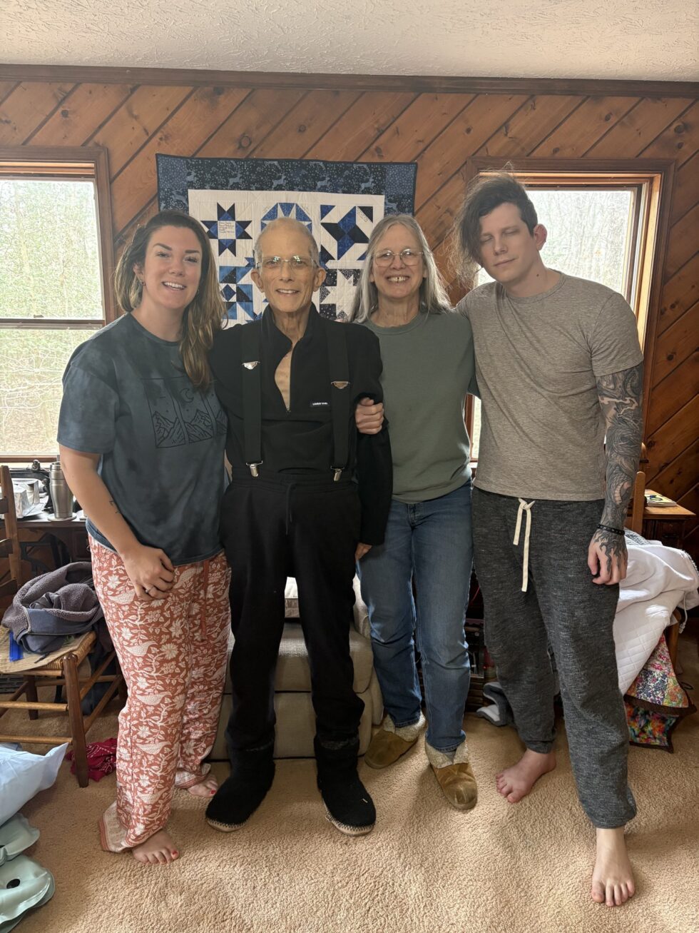 Four family members standing together in a wood panelled living room.