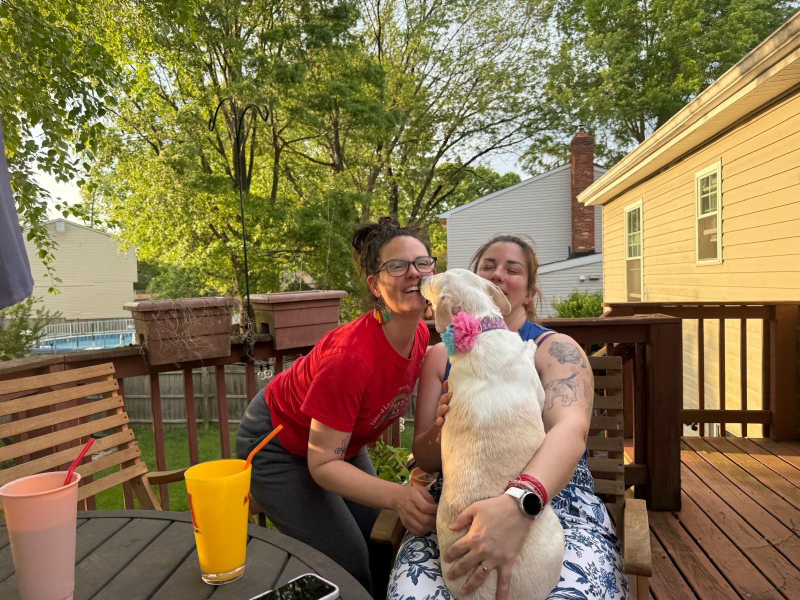 Two friends on a back deck with a white dog between them.
