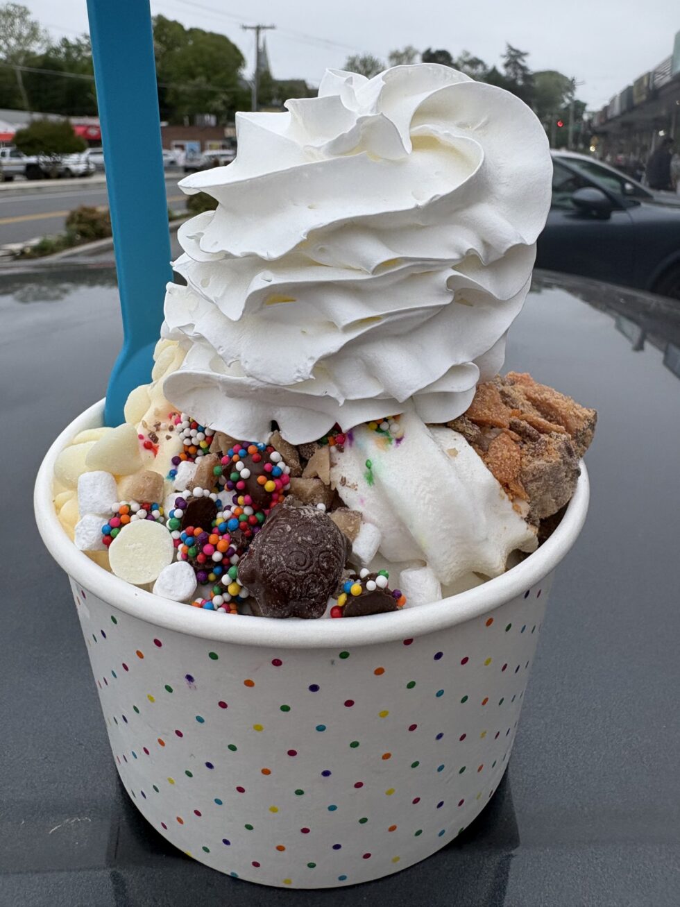 A cup of frozen yogurt piled high with whipped cream, cookie dough and sprinkles.