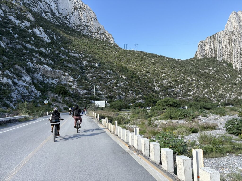 Cyclists riding a paved road toward the limestone peaks of La Huasteca near Monterrey