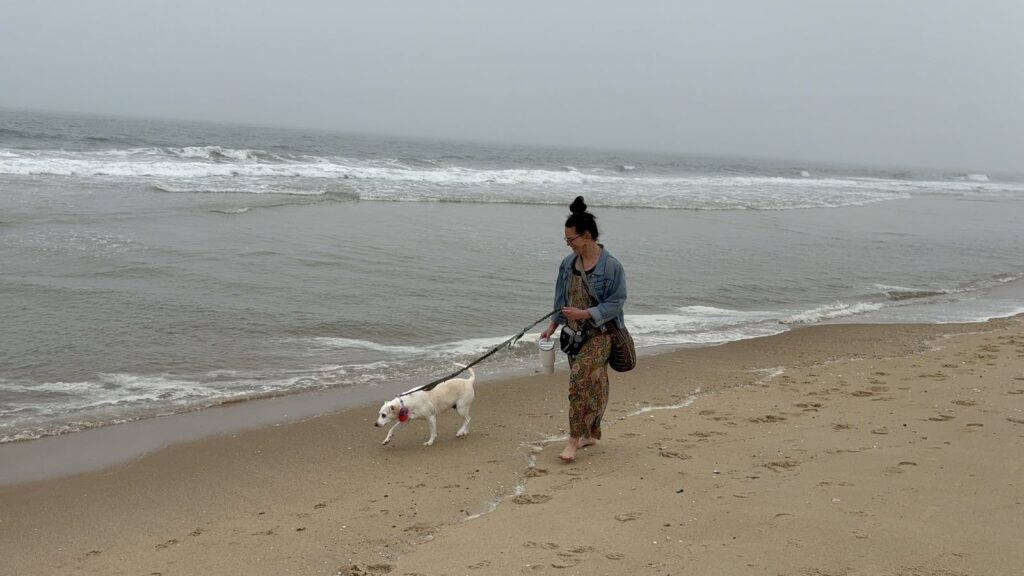 A woman and a white dog at the waterline with fog hiding the horizon