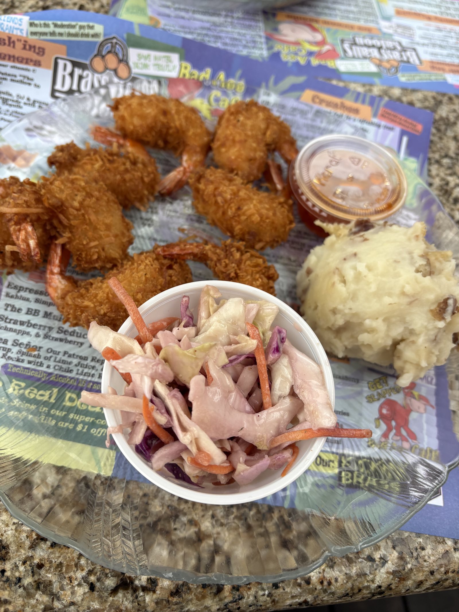 A fried seafood platter with crab, hush puppies and coleslaw on a paper placemat
