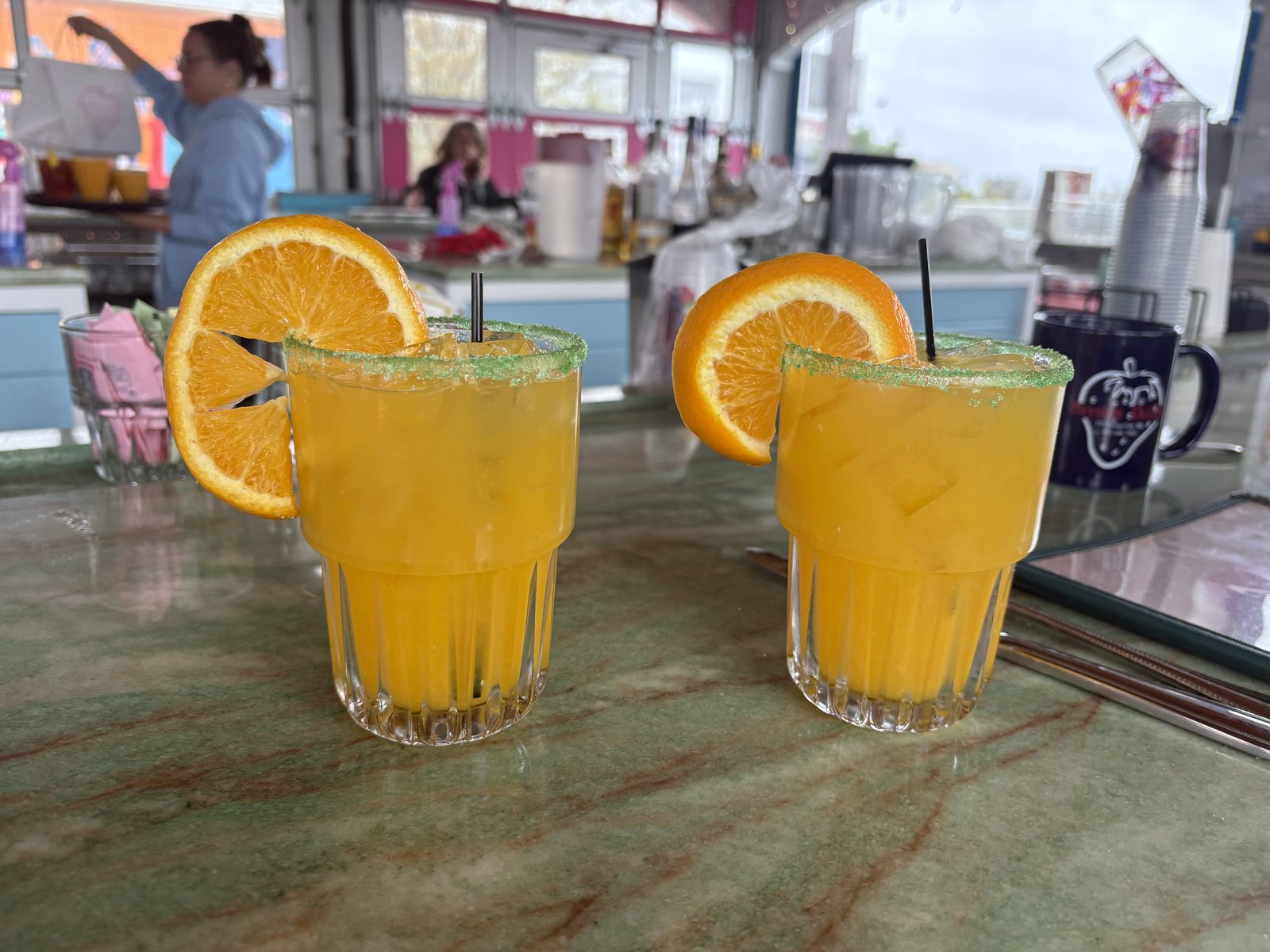 Two Orange Crush cocktails with orange wheels on the rim on a boardwalk bar table