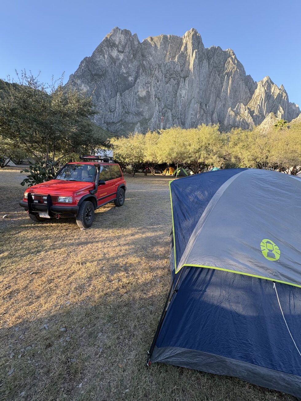 A red SUV and a blue tent at a campground below the limestone peaks of El Potrero Chico