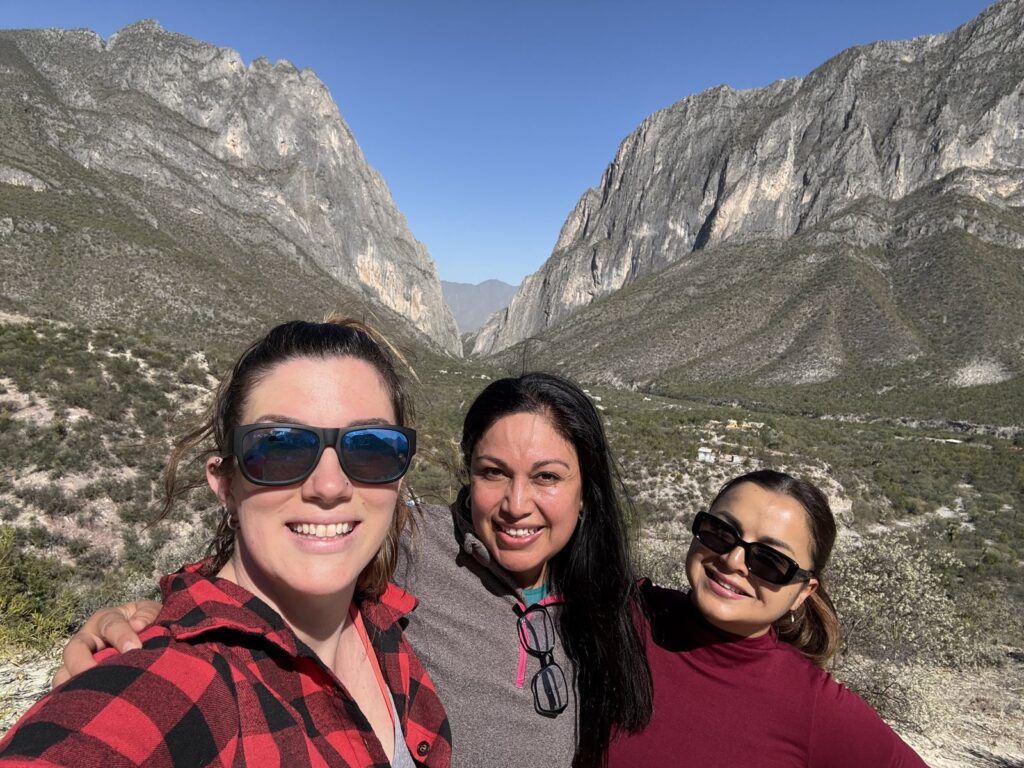 Hannah and two friends smiling on a hillside above the limestone walls of El Potrero Chico