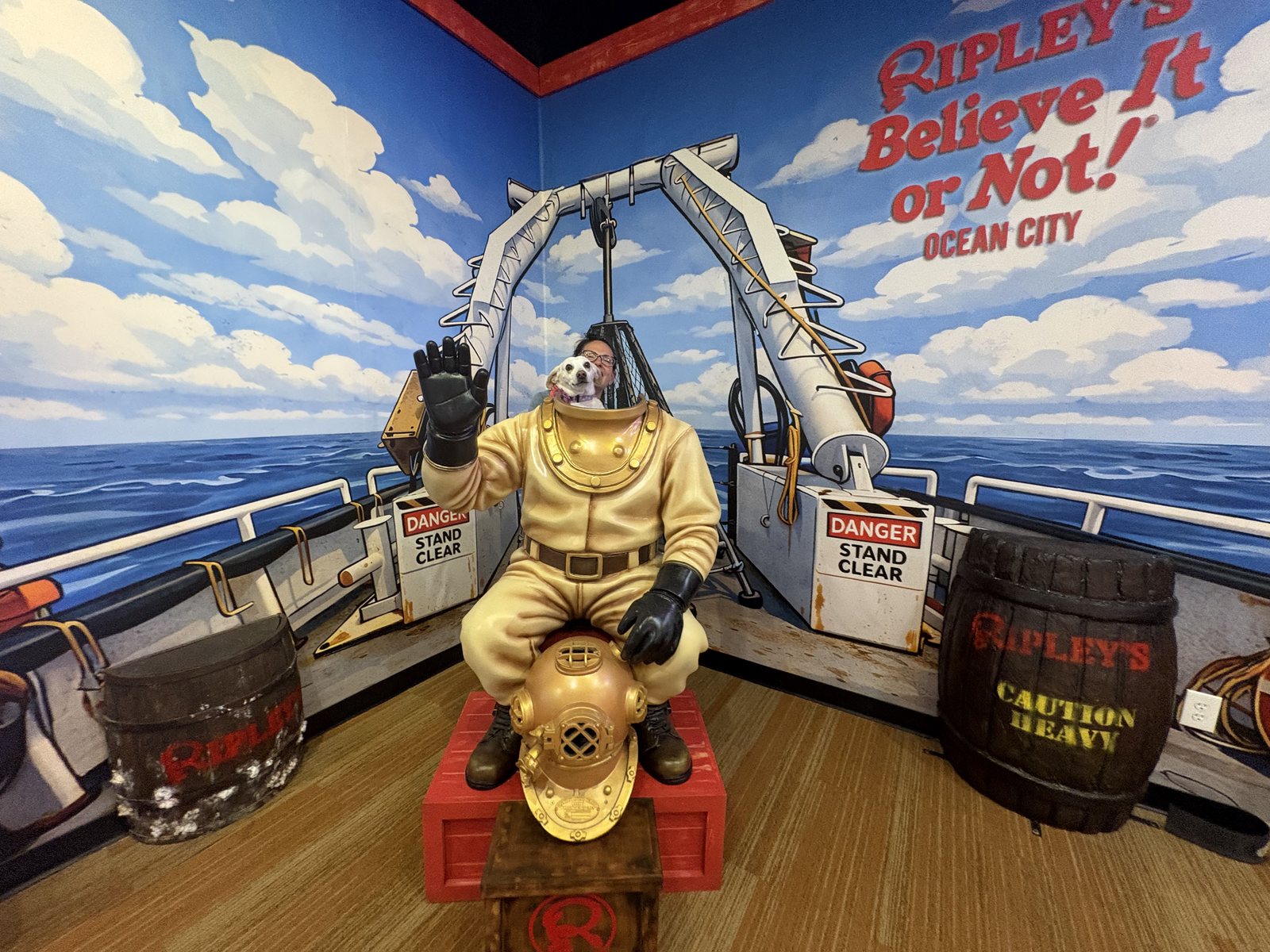 A white dog sitting on a gold deep sea diver statue under the Ripley's Believe It or Not Ocean City sign