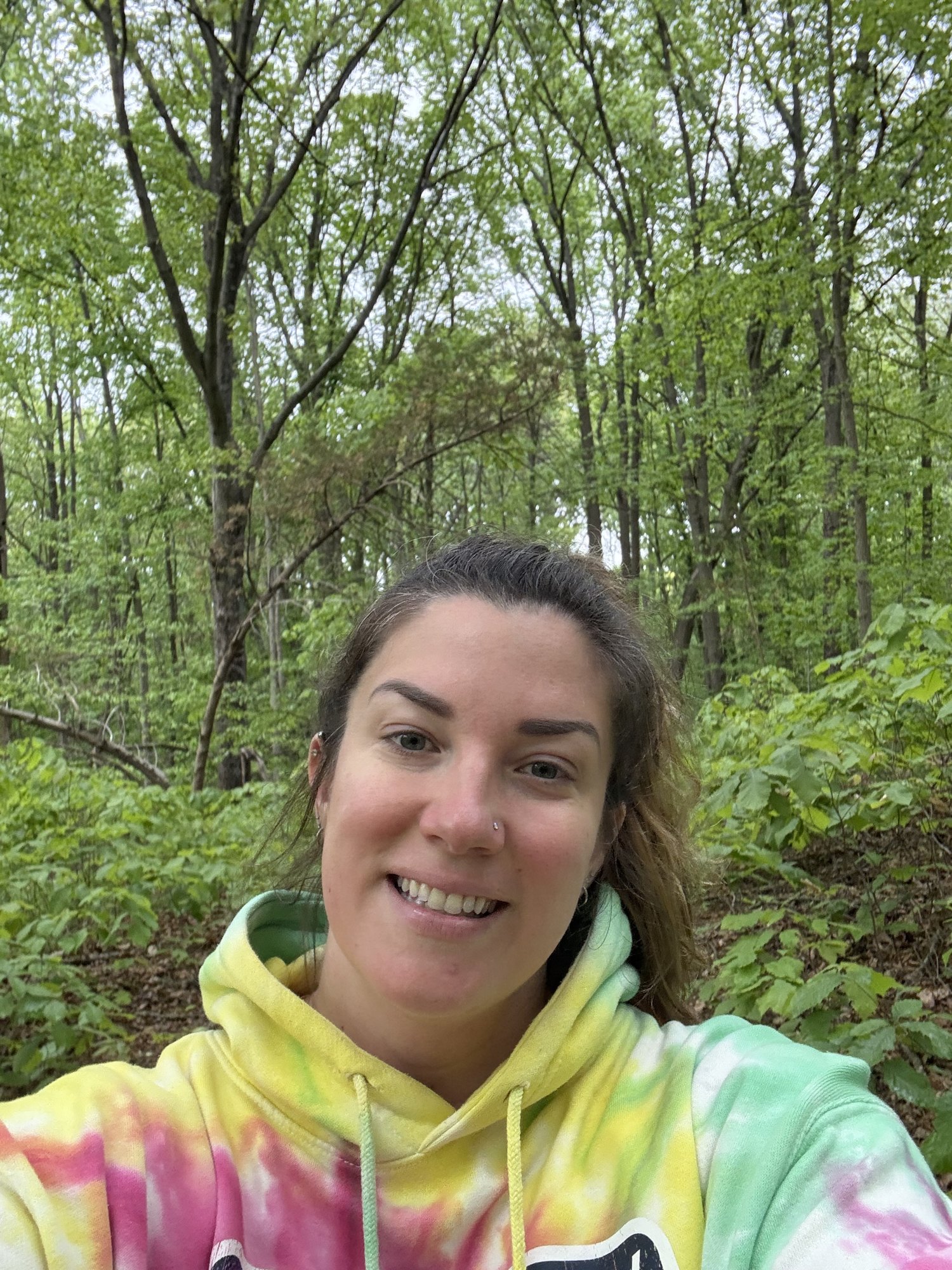 A woman in a tie dye hoodie standing on the wooded trail in Truxtun Park.